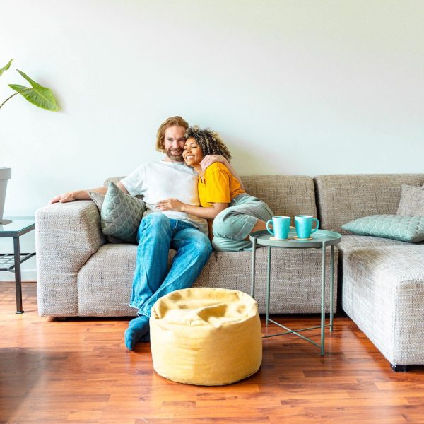 Cheerful multiracial couple sitting on sofa in the living room - Happy family moving in new home - Real estate and stylish furniture concept
